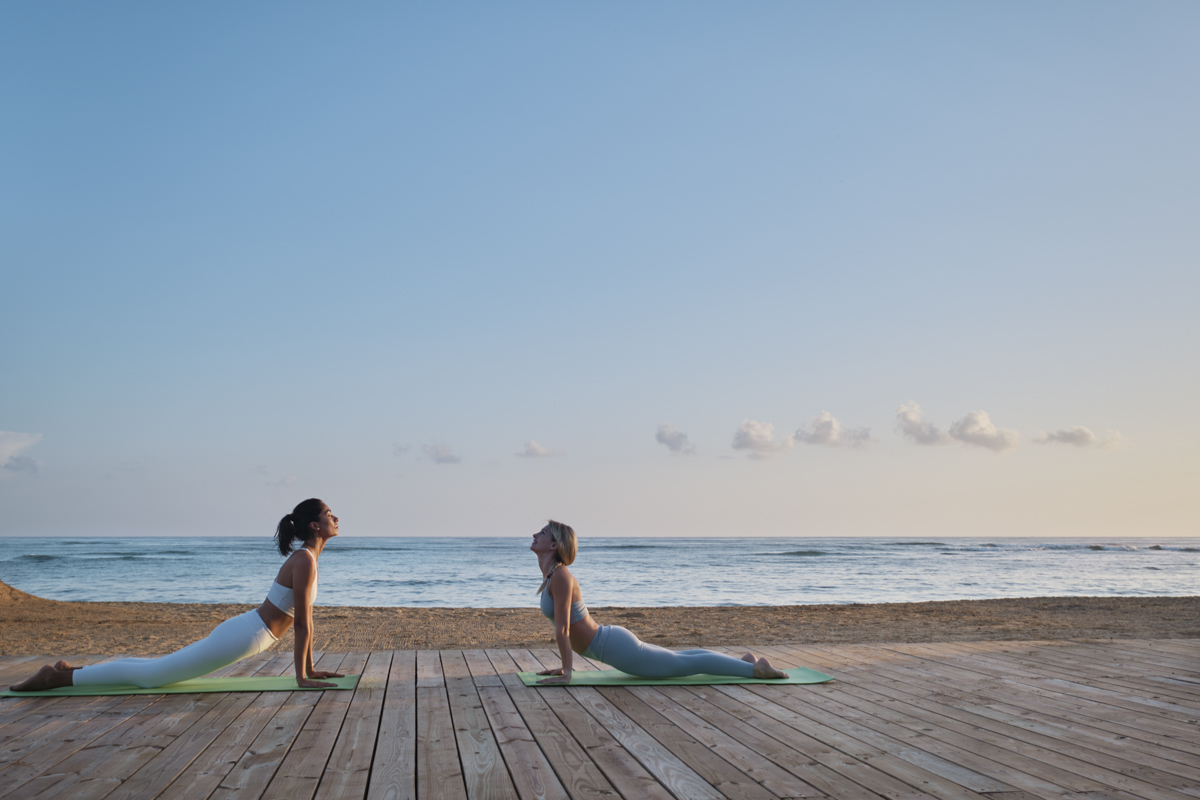 Two women facing each other doing Yoga on the beach in the Caribbean